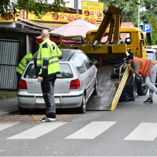 Strażnicy i pracownicy odholowują samochód z ulicy na platformę lawety.