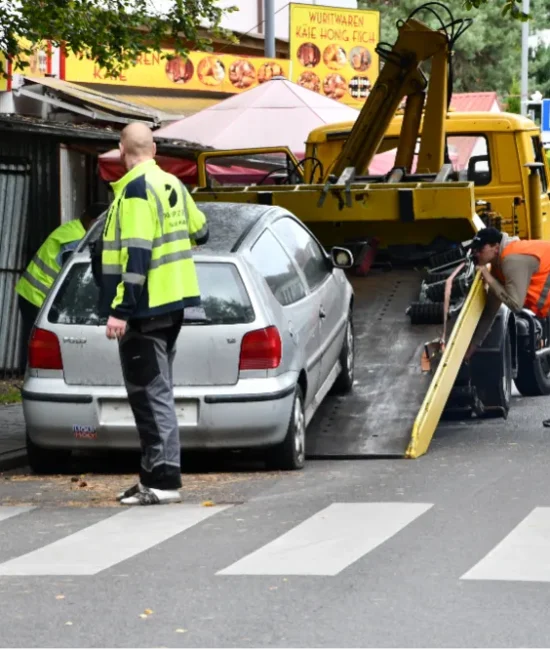 Strażnicy i pracownicy odholowują samochód z ulicy na platformę lawety.