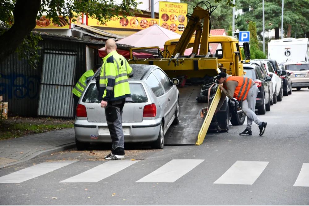 Strażnicy i pracownicy odholowują samochód z ulicy na platformę lawety.