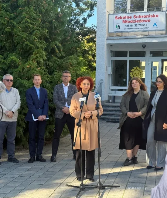 Kilka osób stoi przed wejściem do budynku schroniska młodzieżowego podczas konferencji prasowej.