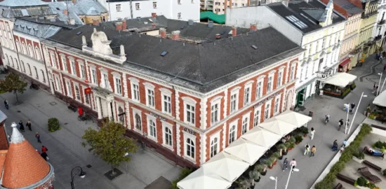 Widok z góry na ceglany budynek przy placu i okoliczną zabudowę miejską.