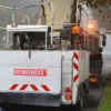 Zamiatarka uliczna na mokrej jezdni przy znaku ograniczenia prędkości.