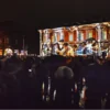 Tłum stoi przed budynkiem poczty podczas nocnego pokazu mappingu 3D.